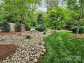 Spacious backyard featuring a rock garden, green grass, trees, and tasteful landscaping at 915 Houston Dr, Monroe, NC 28110