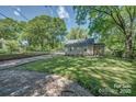 Backyard and driveway featuring mature trees, green grass, and space for outdoor activities at 1308 Lineberger Ave, Gastonia, NC 28052