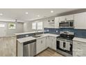 Well-lit kitchen boasts stainless steel appliances, white cabinetry, blue backsplash, and an open floor plan at 109 W Poplar St, Stanley, NC 28164