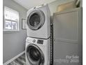 Efficient laundry area with stacked washer and dryer, storage cabinet, window with natural light and grey walls at 901 Heritage Pkwy, Fort Mill, SC 29715
