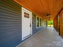 Covered front porch with a wood ceiling, a white door, and views of the surrounding greenery at 3546 Mount Pleasant N Rd, Concord, NC 28025