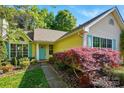 Charming yellow home with lush landscaping, including flowering shrubs, mature trees, and a well-manicured lawn at 6307 Old Corral St, Charlotte, NC 28277