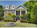 A brick two-story home with white pillars and blue shutters surrounded by green trees and a beautifully landscaped front yard at 9810 Daufuskie Dr, Charlotte, NC 28278