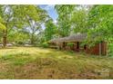 View of a single-story brick home with green lawns, mature trees, and visible 'For Sale' signage at 102 Forest Ct, Huntersville, NC 28078