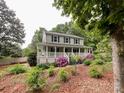 Inviting two-story home with a charming front porch and lush landscaping with blooming pink flowers and mature trees at 2214 Cannonade Ct, Matthews, NC 28105