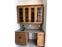 Elegant wet bar with light wood cabinets, glass shelving, and a stylish gray countertop at 6511 Rehobeth Rd, Waxhaw, NC 28173