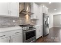 Modern kitchen featuring white cabinets, quartz countertops, a stainless steel range hood, and brick backsplash at 4109 Bryant Terraces Dr, Charlotte, NC 28208
