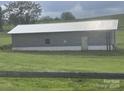 A single story, rectangular storage building featuring concrete block construction and a metal roof, set in a grassy field at 7527 Old Shelby Rd, Vale, NC 28168