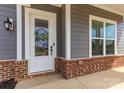 Charming home entrance features a white door with glass and decorative wreath, brick accents and a cozy light fixture at 1358 Cedardale Ln, Denver, NC 28037