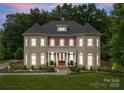 Elegant stone and brick home with a well-lit exterior and manicured lawn at dusk at 7005 Camrose Crossing Ln, Matthews, NC 28104