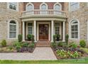 Stunning stone and brick home featuring a columned front entrance, balcony, and landscaped front yard at 7005 Camrose Crossing Ln, Matthews, NC 28104