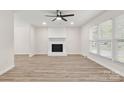 Bright living room featuring wood-look floors, a modern ceiling fan, and a cozy painted white brick fireplace at 7141 Pitchfork Ln, Mint Hill, NC 28227