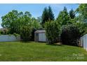Backyard with a shed, green grass, bushes, trees, and a white fence at 1004 Toquima Trl, Monroe, NC 28110