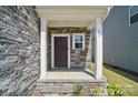 Covered front porch with stone accents, white columns, and a dark wood front door with sidelight window at 637 Scotch Meadows Loop, Monroe, NC 28110