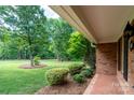 View of the home's brick exterior, mature trees and landscaped front yard from a covered porch at 4145 Wrangler Sw Dr, Concord, NC 28027