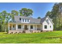 Expansive white farmhouse with a welcoming front porch, lush lawn, and beautiful landscaping at 7768 Lynwood Ln, Sherrills Ford, NC 28673