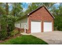 Side view of a brick two-car garage with white doors and light green siding against a backdrop of lush greenery at 2306 Beechwood Dr, Waxhaw, NC 28173