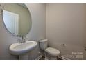 Cozy powder room with a pedestal sink and a round mirror, complemented by neutral wall paint and light wood flooring at 5025 Poplin Vly, Cherryville, NC 28021