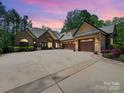 Elegant exterior of home with brick accents, arched entry, and three-car garage under a pink and purple dusk sky at 1579 Sunset Pointe Dr, Salisbury, NC 28146