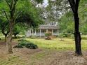 Beautiful front view of a light grey house, surrounded by lush greenery, mature trees, and a well-manicured lawn at 3231 Karen Ln, Monroe, NC 28110