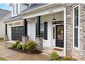 Inviting front porch with stone pillars, black door, manicured landscaping, and a brick and stone facade at 14119 Shelburne Village Dr, Charlotte, NC 28278