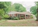 Inviting brick home featuring a covered porch, complemented by mature trees and vibrant flowerbeds at 2412 Wedgewood Dr, Salisbury, NC 28146