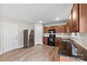 Well-lit kitchen with wood cabinets, stainless steel refrigerator, black appliances, and light wood-look flooring at 614 Oldham Ln, Rock Hill, SC 29732