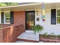 Welcoming front porch with brick accents, a decorative flag, and a potted fern at 4361 Applegate Rd, Charlotte, NC 28209