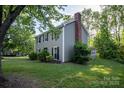 View of the home from the left, featuring a brick chimney and lush green trees at 9801 Kent Village Dr, Charlotte, NC 28269