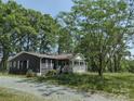 Quaint home with a covered porch and gravel driveway surrounded by lush green trees and vegetation at 1820 Trinity Church Rd, Monroe, NC 28112