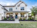 Charming two-story home featuring a welcoming front porch with stone accents and manicured landscaping at 405 Winding Oaks Se Ln, Concord, NC 28025