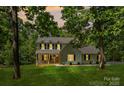 Charming two-story home with light yellow siding, black shutters, and a welcoming front porch, nestled among lush trees at 1338 Pell Dr, Lincolnton, NC 28092