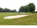 Picturesque view of a well-maintained golf course featuring a sand bunker and mature trees on a cloudy day at 18920 Peninsula Club Dr, Cornelius, NC 28031