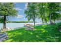 Green backyard featuring mature trees, a fire pit, a boat dock and lake views, and a white picket fence at 4960 Longfield St, Claremont, NC 28610
