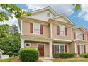 Inviting townhouse featuring red door and shutters, set amongst mature trees and manicured bushes at 8259 Carob Tree Ln, Charlotte, NC 28215