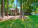 View of a two story house with neutral siding, black shutters, and green lawn surrounded by mature shade trees at 2600 Kirkholm Dr, Matthews, NC 28105
