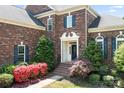 Elegant brick home featuring a well-manicured lawn and vibrant landscaping around the entrance at 7525 Blackgum Falls Ct, Huntersville, NC 28078