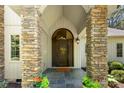 Covered front porch featuring stone pillars and a beautiful arched wood front door at 6599 Majestic Pine Dr, Vale, NC 28168