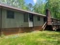 A shot of the rear exterior displaying a brick foundation, wood siding, deck, and mature trees at 1502 Shelby Hwy, Cherryville, NC 28021