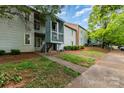 View of the light-grey two-story condo with trimmed shrubbery, stairs to the second floor entrance, and tree coverage at 2026 Harvest Ln, Charlotte, NC 28210