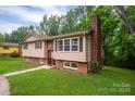 View of the split-level house with brick chimney, green lawn, and mature trees at 2474 Cedar Valley Dr, Conover, NC 28613