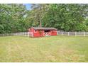 Red barn on a lush green lawn enclosed by a white fence, adding rural charm at 6910 Birdsong Ln, Waxhaw, NC 28173
