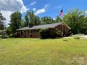 A cozy brick home is nestled on a green lawn with mature trees and an American flag at 211 Amos Homesley Rd, Cherryville, NC 28021