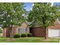 View of the brick and stone facade with dark shutters, manicured lawn, and trees at 2910 Lake James Ct, Monroe, NC 28110