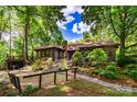 A log cabin nestled among mature trees featuring stone chimney, landscaping, and serene setting at 6510 Sharon Hills Rd, Charlotte, NC 28210