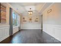 Open dining room featuring dark hardwood floors, large window, decorative tray ceiling and wainscoting at 5105 Paisano Ln, Waxhaw, NC 28173