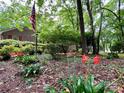 Landscaped front yard with blooming flowers, mature trees, and an American flag at 1623 Arbor Way, Albemarle, NC 28001