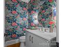 Stylish powder room featuring vibrant floral wallpaper, a round mirror, and a sleek vanity with elegant fixtures at 19614 Meta Rd, Cornelius, NC 28031