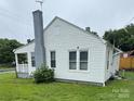 Side view of a single-story home featuring white siding and a grey painted brick chimney at 247 E Cabarrus Ave, Concord, NC 28025