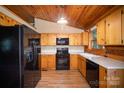 Functional kitchen featuring wood cabinets, black appliances, and wood-look floors in a log cabin home at 8464 Robinson Church Rd, Charlotte, NC 28215